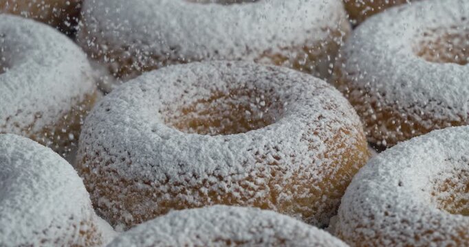Icing sugar dusting over line of fresh donuts at 1000fps. Sweet bakery pattern, golden fried texture, delicious snow effect and morning treat.