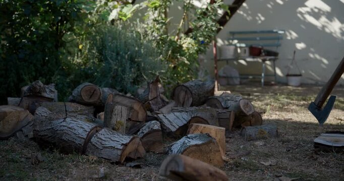 Large axe striking a tree log during firewood preparation in a rustic backyard. Autumn morning light, chopped wood, manual labor and traditional heating preparation concept. 4K slow motion.