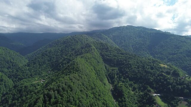 4K drone shot gains altitude above forested ridges in Adjara, Georgia. Passes village houses on slopes, climbing toward clouds near Keda municipality on summer solstice. Original unedited video.