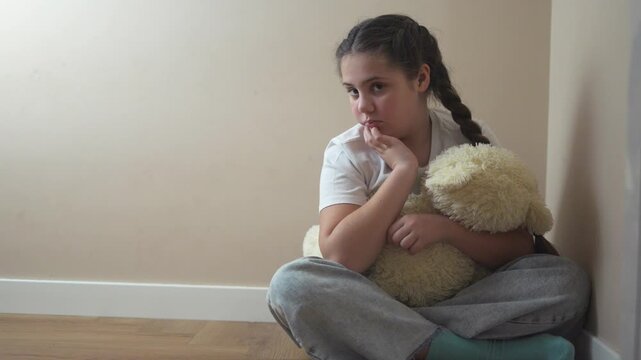Young girl sitting on the floor with teddy bear. Teddy bear punished by sad corner. Teenage girl is traumatized by a violent attack by a teenager. A lifestyle young girl is seated on the floor with a.