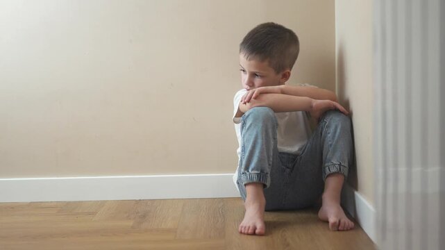 Young girl sitting on the floor. Sad child sits on lifestyle a corner and is punished. A teenage girl is traumatized by a violent incident. A little girl sitting on the ground.