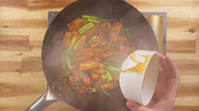Pouring soy based seasoning sauce over Sichuan Twice Cooked Pork and garlic sprouts in a wok.