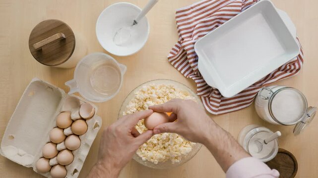 Chef cracking raw eggs into cottage cheese bowl for baking curd casserole. Top view preparing homemade dessert recipe ingredients, sweet breakfast, baking food. High quality 4k footage