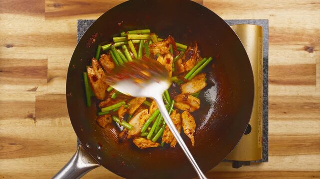 Stir-frying Twice Cooked Pork with fresh garlic sprouts and spicy broad bean paste in a hot wok. Real-time Asian cooking showcasing authentic Sichuan cuisine.