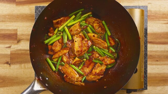 Stir-frying Twice Cooked Pork with fresh garlic sprouts and spicy broad bean paste in a hot wok. Real-time Asian cooking showcasing authentic Sichuan cuisine.