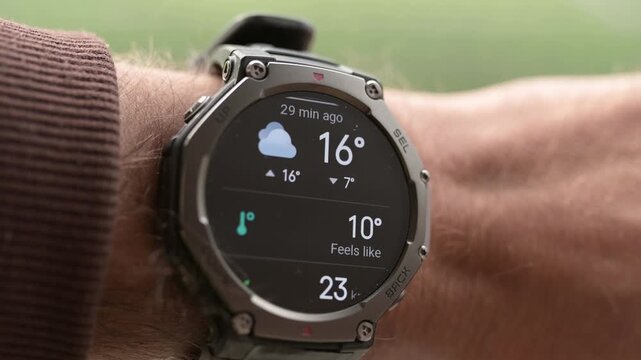 Close-up of rugged smartwatch on wrist showing weather forecast and temperature