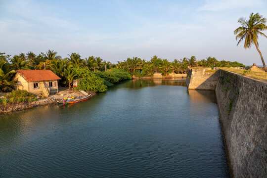 Moat beside an old fort stone wall with a house among palm trees, Northern Province, Mannar, Sri Lanka