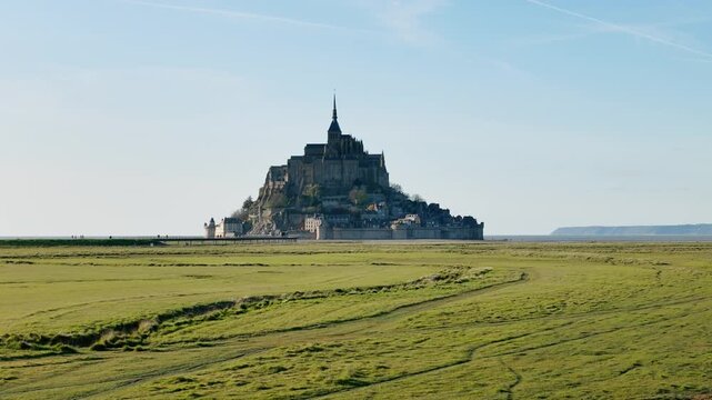 Mont Saint Michel abbey and fortified village in Normandy, France. Distant footage of historic island architecture across salt marsh meadows for French heritage
