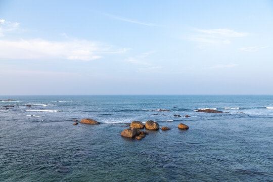 Calm blue sea with rocks and small waves under a pale sky, Southern Province, Galle, Sri Lanka