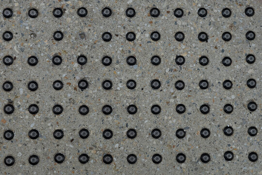 Tactile Warning Studs on Concrete Pavement Horizontal Background &mdash; overhead view of black metal domes in rows on speckled aggregate for visually impaired pedestrians, wide accessibility pattern banner