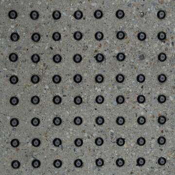 Square Tactile Warning Studs on Concrete Pavement Background &mdash; overhead view of black metal domes in a grid on speckled aggregate, accessibility pattern for social media and tiles