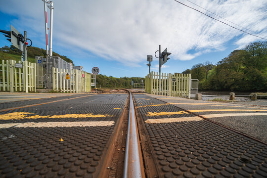 View of the level crossing at Terras Bridge with railway tracks, safety barriers, and warning signs in Looe, England, United Kingdom.