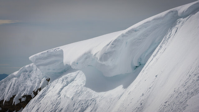 View of a dramatic snow cornice on a mountain ridge in the Jura mountains, with deep snow cover and clear winter light, Crozet, Auvergne-Rhone-Alpes, France.
