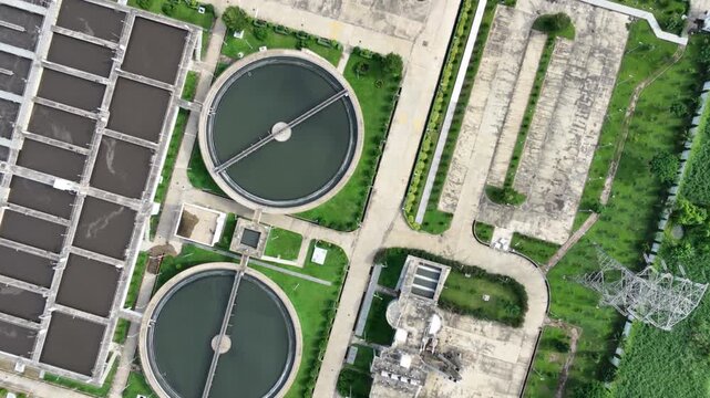 Top-down aerial forward flight over sewage treatment plant with circular clarifier tanks, settling basins and water discharge into wetland, Dhaka, South Asia