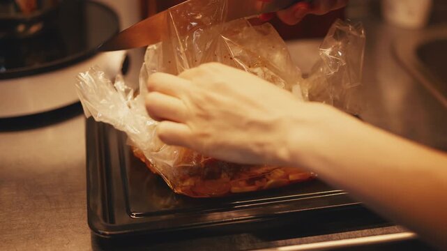 Chef cuts open an inflated roasting bag with a knife on a baking sheet to reveal cooked duck breast fillets. Close-up of freshly roasted poultry in a kitchen. Ready to serve for a home dinner.