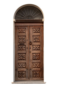 Old rustic brown wooden double door featuring intricate geometric star and cross carvings. Entry door is built with a classic round arch, wrought iron sunburst transom window grille at top