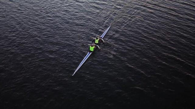Drone view of rowing athletes training early in the morning on Halifax Harbour, Canada, with women and men rowing single and double racing shells beneath the rising sun.