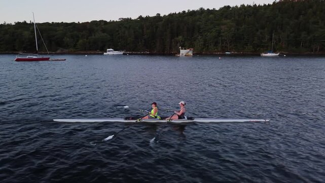 Aerial cinematic shot of rowing athletes training in Halifax, Nova Scotia, Canada, with single and two-person racing boats gliding across the harbour as the sun rises.