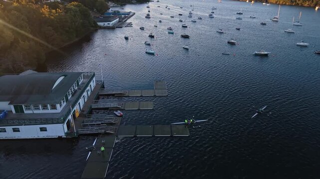 Aerial view of rowers finishing practice at a coastal rowing center in Halifax, Canada, with athletes working together to pull their racing boats onto a wooden pier.