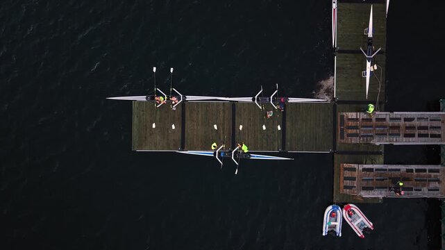 Cinematic drone footage of a rowing sports center in Halifax, Nova Scotia, showing athletes on a wooden dock lifting long racing shells from the water after an ocean training session.