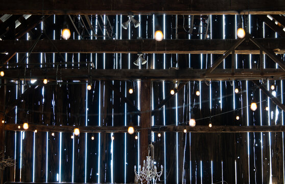 Inside a dark barn looking out at the sunlight through the  gaps in the wooden slats of the rustic walls.