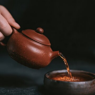 Hand pouring amber tea from a rounded terracotta teapot