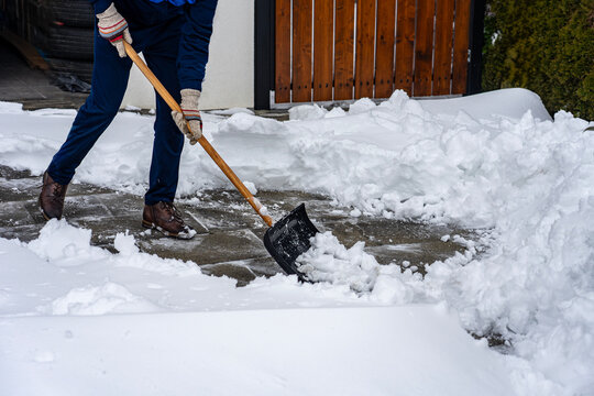 erson clearing heavy snow from residential driveway with snow shovel
