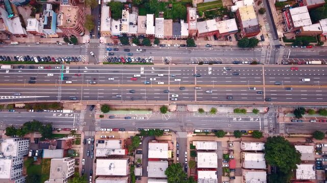 Traffic crosses a New York neighborhood on an elevated roadway. An overhead view shows parallel streets and white rooftops beside lanes marked with arrows.