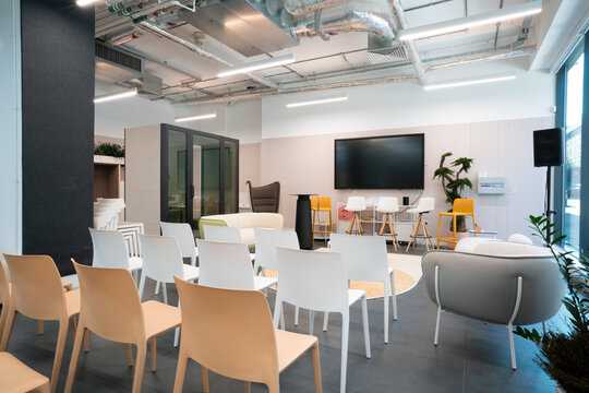 View of the modern Office Mix event space featuring rows of white chairs, a large wall-mounted screen, and minimalist furniture in London, United Kingdom.
