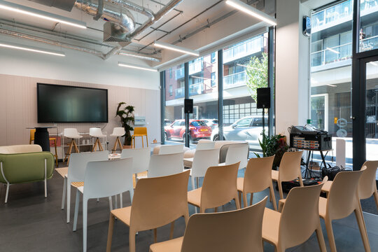 View of the Office Mix event space featuring rows of modern chairs, a large wall-mounted screen, and floor-to-ceiling windows overlooking a city street in London, United Kingdom.