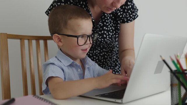 home online education concept. mother helping child use computer laptop first time. studying online together parent help kid baby boy learn online. happy preschooler boy learning type keyboard