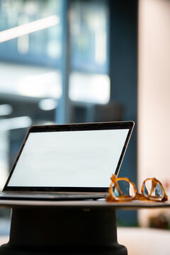 View of a laptop with a blank screen sitting on a desk next to a pair of glasses in a modern office, London, United Kingdom.