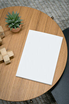 View of a blank white notebook resting on a round wooden table alongside a small potted succulent and wooden decorative objects in London, United Kingdom.