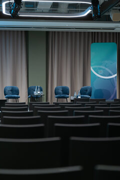 View of a stage setup with blue chairs and a branded backdrop in a conference room in London, United Kingdom.