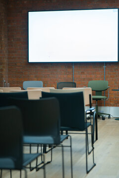 View of a modern meeting room with rows of chairs facing a large blank screen mounted on an exposed brick wall in London, United Kingdom.