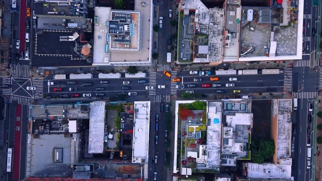 Traffic passes through a Manhattan intersection between city blocks. White rooftops frame striped crosswalks and yellow taxis in a direct overhead view.