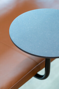 View of a modern circular side table with a textured blue top and a black metal base positioned next to a brown leather surface in London, United Kingdom.