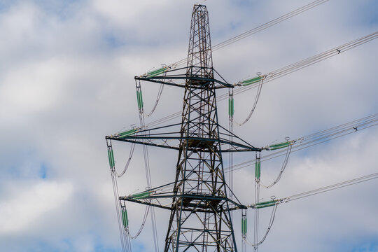 View of a metal electricity transmission tower with power lines and insulators against a cloudy sky in Deeside, Wales, United Kingdom.