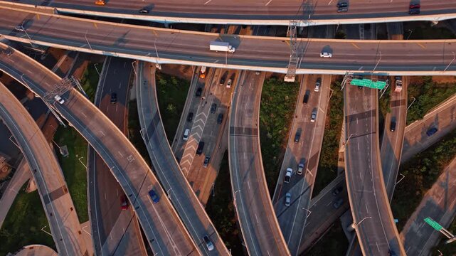 Multiple overpasses overlap above highway lanes in New York. Cars follow branching ramps marked with white lines as low light casts shadows across the roads.