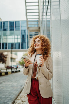 Young businesswoman smiling enjoying coffee and smartphone outdoors
