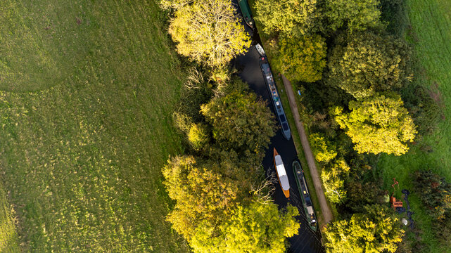 Narrowboats docked on a peaceful, sunlit rural canal in autumn.