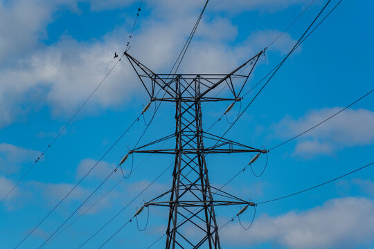 View of a steel electricity transmission pylon with power lines against a bright blue sky with scattered white clouds in Deeside, Wales, United Kingdom.