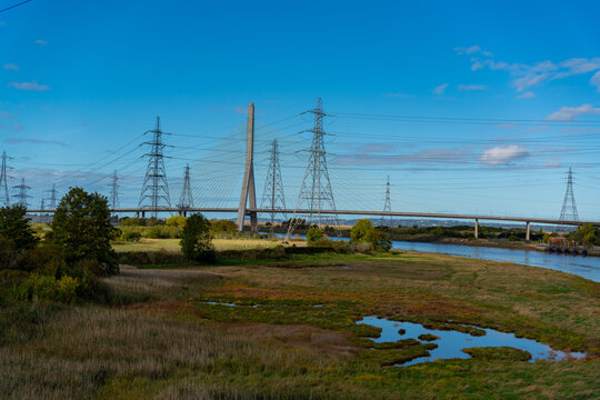 View of the cable-stayed Flintshire Bridge spanning the River Dee, surrounded by high-voltage electricity pylons, marshland, and lush greenery in Deeside, Wales, United Kingdom.