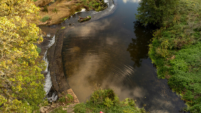 Water cascades over Warleigh Weir in a scenic autumn woodland river.