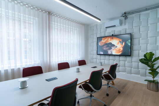 View of a modern meeting room with a long white table, red office chairs, a large wall-mounted screen, and acoustic wall paneling in London, United Kingdom.