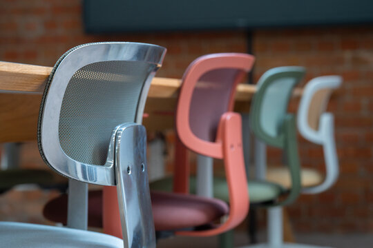 View of a row of colorful modern office chairs with mesh backs arranged in a meeting room with a brick wall background in London, United Kingdom.