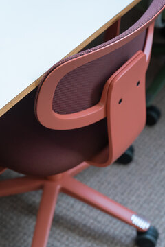 View of a modern ergonomic office chair with a terracotta-colored frame and mesh backrest positioned next to a white desk in a professional workspace in London, United Kingdom.