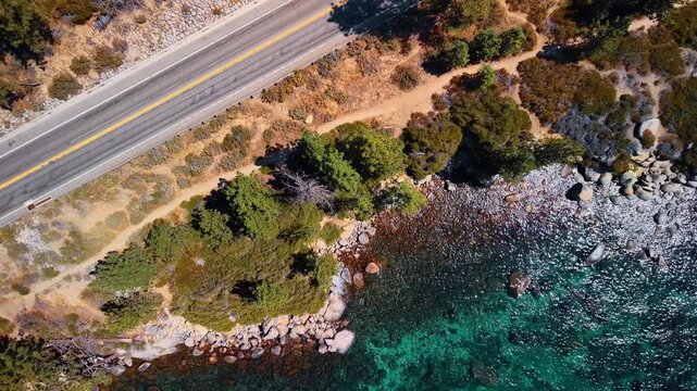 A road parallels the rocky edge of Lake Tahoe. An overhead view pairs gray asphalt with a footpath and green shrubs beside turquoise water.