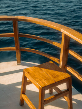 View of a wooden stool on the deck of a boat with a wooden railing overlooking the deep blue sea in Komodo National Park, Komodo, Nusa Tenggara Timur, Indonesia.