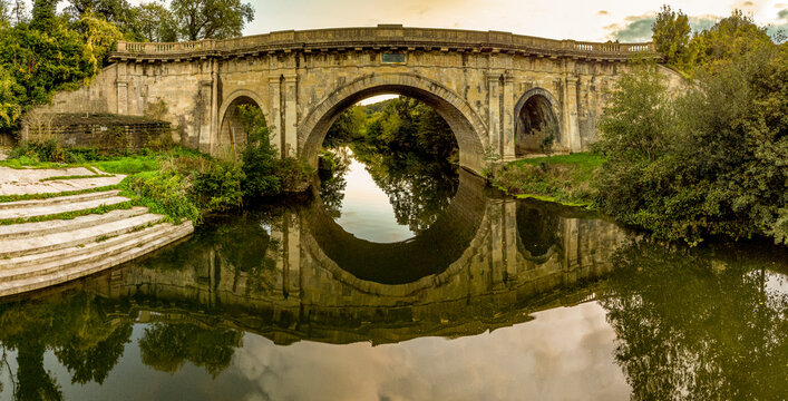 Dundas Aqueduct reflects in calm water near Bath, England, at sunset.